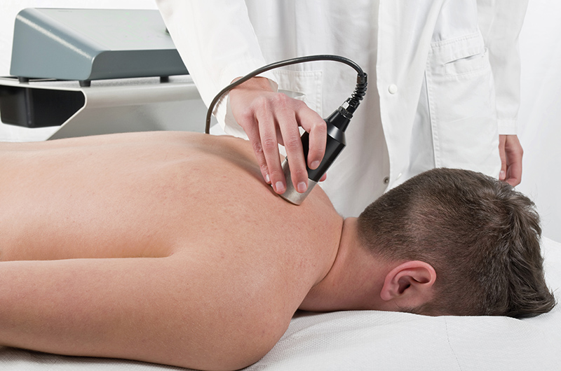 Fysioterapeutti antaa ultraäänihoitoa potilaan yläselän lihaksiin.